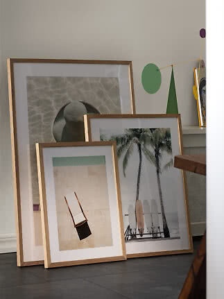 Three framed art prints leaning against a wall in a bright room