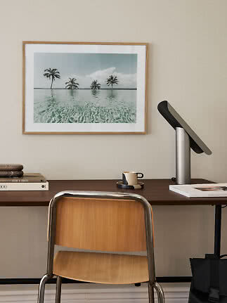 Schreibtisch mit Holzstuhl, Tischlampe und gerahmtem Palmenbild an der Wand