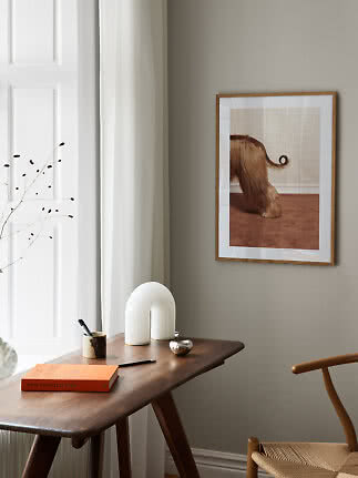 Indrammet kunstplakat med brun, langhåret hund på beige væg over træbord