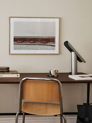 Wooden desk with chair, black table lamp and framed photo on a beige wall