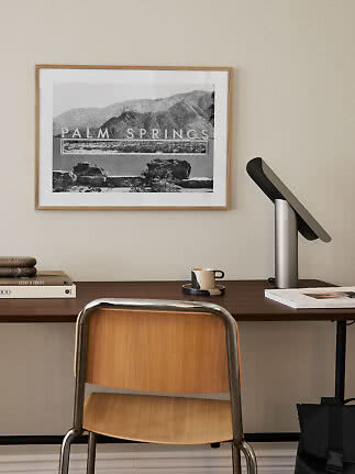 Schreibtisch mit Holzstuhl, Tischlampe und gerahmtem Palm-Springs-Poster an beiger Wand