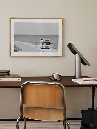 Skrivebord med træstol, sort bordlampe og indrammet sort-hvidt foto på beige væg