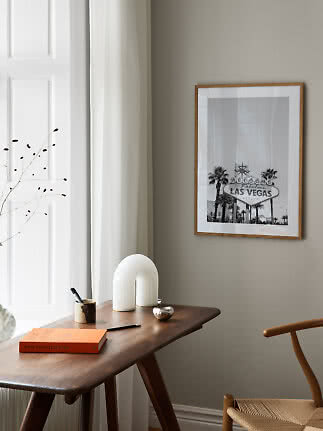 Indrammet sort-hvid Las Vegas-plakat over et træskrivebord i et lyst, minimalistisk rum