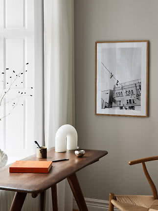 Framed black-and-white print on beige wall above a wooden desk in a bright minimalist room
