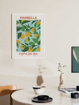 Framed Marbella poster with lemons and green leaves on a light wall above a round table