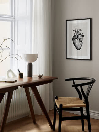 Framed anatomical heart print on wall above wooden desk and black chair in a bright minimalist room