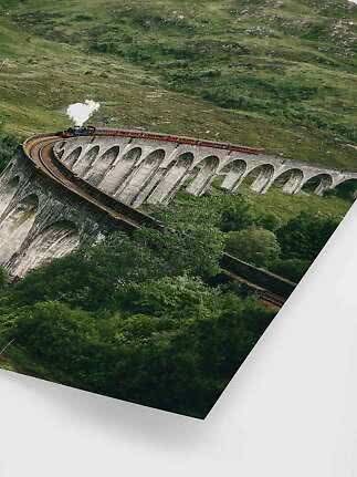 Steam train crossing a curved stone viaduct in a green hillside landscape