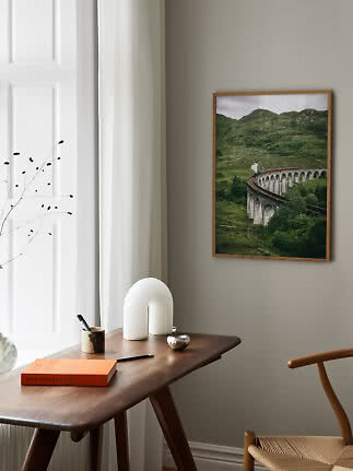 Framed poster of a steam train on a stone viaduct in green hills above a wooden desk