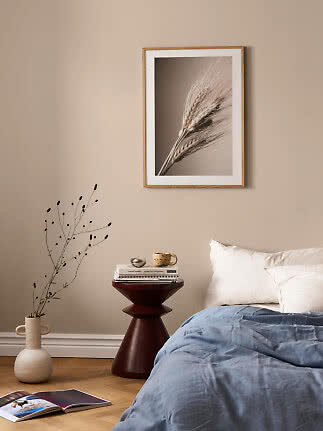 Poster incorniciato con primo piano di spighe sopra un letto in una camera beige