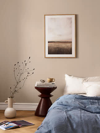 Chambre avec couette bleue, table d’appoint foncée, vase et affiche de champ encadrée sur mur beige