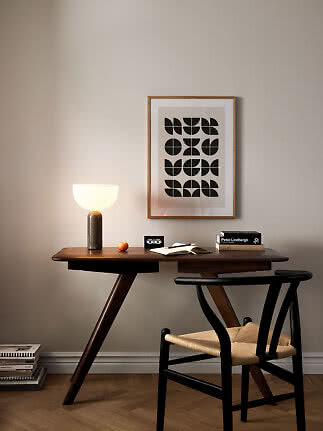 Schreibtisch aus dunklem Holz mit leuchtender Tischlampe, Stuhl und grafischem Wandbild