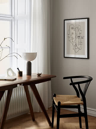 Minimalistisk hjemmekontor med træskrivebord, sort stol, bordlampe og abstrakt vægkunst ved vindue