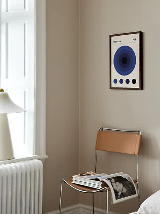 Indrammet Bauhaus-plakat med blå cirkler hænger over en brun læderstol i et lyst hjørne
