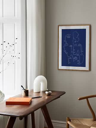 Lámina azul enmarcada con rostros abstractos sobre una mesa de madera en una estancia luminosa