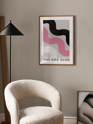 Ingelijste abstracte poster met zwarte en roze golven aan beige muur boven een crèmekleurige stoel