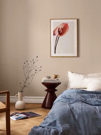 Schlafzimmer mit gerahmtem Blumenbild über dem Bett, blauer Decke und dunklem Beistelltisch