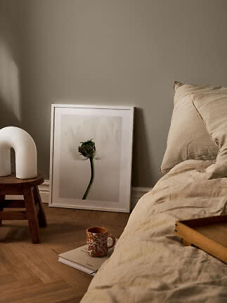 Camera da letto accogliente con biancheria beige, stampa floreale a terra e lampada bianca