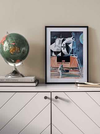 Gerahmtes Poster mit Mondlandefähre auf einem Sideboard neben einem Globus