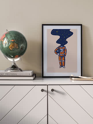 Indrammet plakat med astronautmotiv på skænk ved siden af en globus.