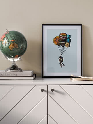 Indrammet plakat med astronaut, der holdes oppe af planeter, stående på hvid kommode ved siden af en globus