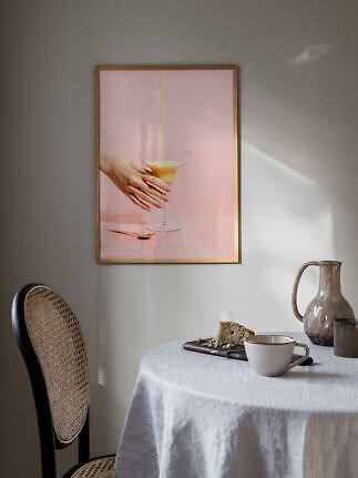 Affiche encadrée au-dessus d’une table, image rose d’une main, d’un verre et d’une boisson versée