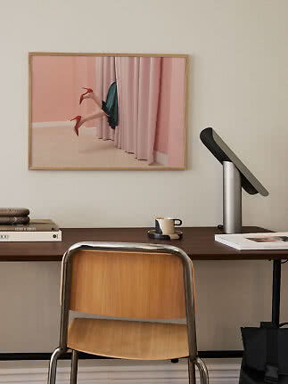 Inramad konstbild över skrivbord med ben i röda klackar bakom rosa gardiner