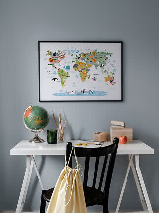 Framed world map poster above a desk with globe, paintbrushes, notebook, and black chair.