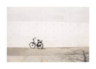 Schwarzes Citybike mit Korb vor einer großen hellen Betonwand geparkt