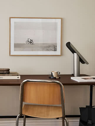 Homeoffice mit Holzstuhl, dunklem Schreibtisch, Tischlampe und gerahmtem Fahrradbild an der Wand