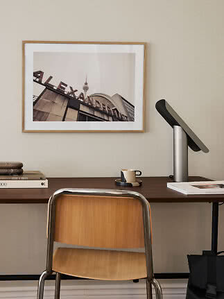 Dunkler Holzschreibtisch mit Stuhl, Lampe, Büchern, Tasse und gerahmtem Fotodruck an der Wand
