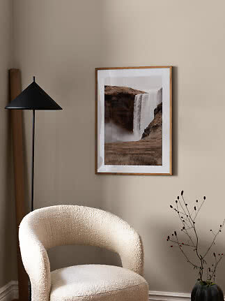 Indrammet plakat med vandfald i træramme på beige væg over en cremefarvet stol