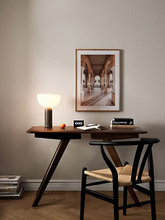 Scrivania in legno scuro con sedia, lampada da tavolo accesa e stampa architettonica incorniciata