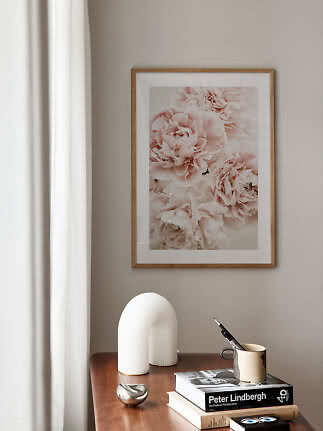 Stampa floreale incorniciata con peonie rosa sopra un tavolo in legno con libri e oggetti decorativi