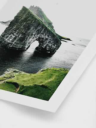 Photo of a green rock formation with a natural arch over the sea