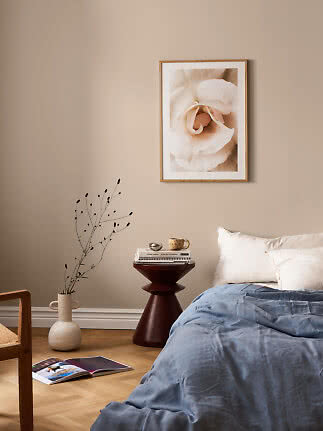 Schlafzimmer mit blauer Bettdecke, weißen Kissen, rundem Beistelltisch und Blumenbild an beiger Wand