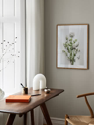 Stampa botanica con cornice in legno su parete beige sopra una scrivania minimalista