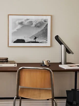 Home office with wooden chair, desk lamp, and framed black-and-white surfer print on the wall
