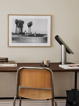 Modern desk with wooden chair, black table lamp, and framed black-and-white photo on the wall