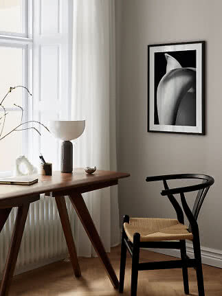 Angolo lavoro minimalista con scrivania in legno, sedia nera, lampada da tavolo e stampa in bianco e nero