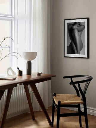 Black-framed black-and-white art print above a wooden desk by a window