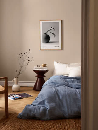 Cozy bedroom with blue duvet, wooden side table and framed botanical poster on beige wall