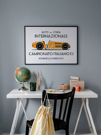 Framed poster of a yellow vintage race car above a white desk against a gray wall