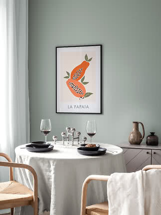 Ingelijste papajaposter boven gedekte eettafel met zwarte borden en wijnglazen