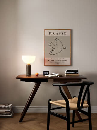 Dunkler Holzschreibtisch mit schwarzem Stuhl, leuchtender Lampe und gerahmtem Picasso-Poster