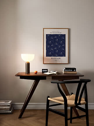Skrivebord i mørkt træ med bordlampe, bøger, notesbog og sort stol under blå plakat på væggen