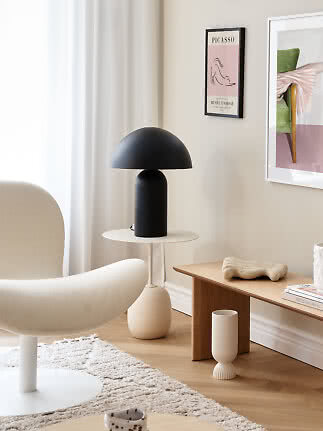 Black dome table lamp on a round white side table in a bright modern living room corner.