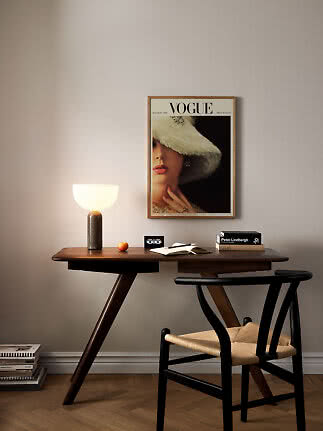 Mörkt träbord med bordslampa, böcker och stol under en inramad Vogue-affisch