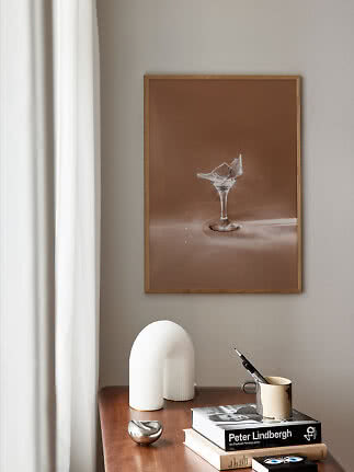 Gerahmtes Poster mit zerbrochenem Glas an beigefarbener Wand über Holztisch mit Büchern und Tasse