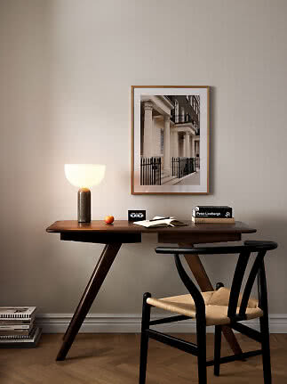 Scrivania in legno scuro con sedia nera, lampada da tavolo accesa e stampa architettonica incorniciata