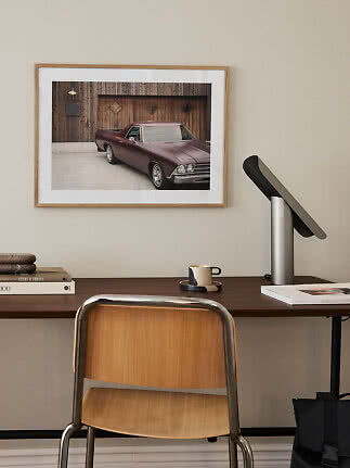 Home office with wooden chair, desk lamp, and framed photo of a classic car on the wall